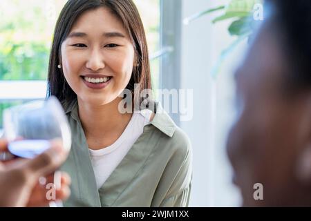 Jeune femme adulte souriant tout en parlant avec un ami tout en buvant du vin Banque D'Images