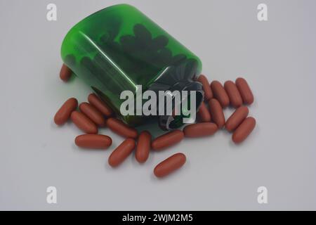 Médicaments, pilules, médicaments, pot vert avec des vitamines coûteuses rempli de capsules brunes, comprimés liquides et couvercle en plastique blanc placé sur blanc. Banque D'Images