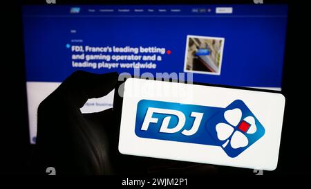 Personne tenant smartphone avec logo de la société française de loterie française des Jeux (FDJ) en face du site. Concentrez-vous sur l'affichage du téléphone. Banque D'Images