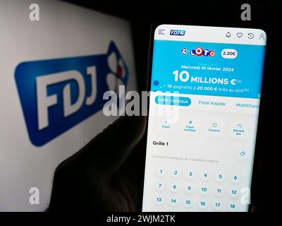 Personne tenant le téléphone portable avec la page web de la société française de loterie française des Jeux (FDJ) devant le logo. Concentrez-vous sur le centre de l'écran du téléphone. Banque D'Images