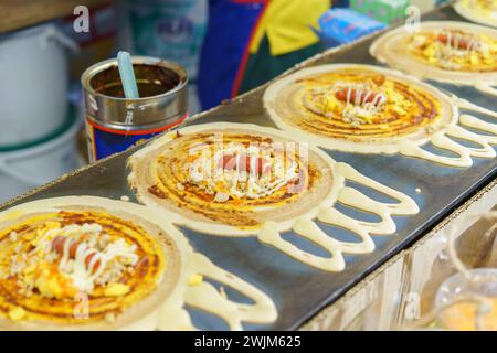 Des crêpes croustillantes de style thaïlandais fraîchement préparées, connues sous le nom de « Kanom Tokyo », sur une plaque chauffante, garnies d'œufs et de saucisses. Banque D'Images