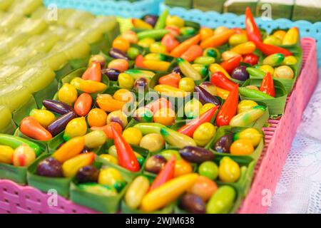 Un assortiment de haricots mung en forme de fruits, des desserts thaïlandais vibrants, conçus pour ressembler à des fruits et légumes miniatures, présentés dans des récipients transparents à Banque D'Images