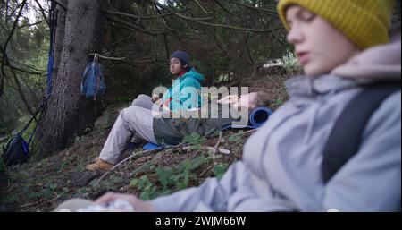 Mouvement lent de couple multiethnique de voyageurs parlant, ayant une collation dans les bois pendant le voyage touristique ou la randonnée, regardant le paysage. Randonneurs se reposant après un long trek en montagne. Concept de loisirs actifs Banque D'Images