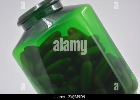 Médicaments, pilules, médicaments, pot vert avec des vitamines coûteuses rempli de capsules brunes, comprimés liquides et couvercle en plastique blanc placé sur blanc. Banque D'Images