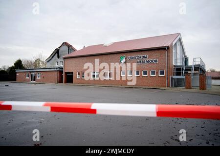 Neermoor, Allemagne. 16 février 2024. Une barrière est suspendue devant le club-House SV Concordia Neermoor et la salle de sport de l'école primaire incendiée (l) dans le village. Un incendie a détruit le gymnase de l'école primaire de Neermoor hier soir. Des vents violents et des matériaux de construction facilement combustibles dans le hall ont fait que le feu s'est propagé en un incendie plus grand avec des étincelles volantes et de la fumée lourde. Crédit : Hauke-Christian Dittrich/dpa/Alamy Live News Banque D'Images