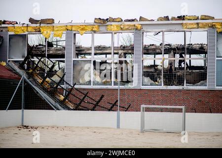 Neermoor, Allemagne. 16 février 2024. Des matériaux de construction pendent du toit du gymnase de l'école primaire incendiée à Neermoor. Un incendie a détruit le gymnase de l'école primaire de Neermoor hier soir. Des vents violents et des matériaux de construction hautement inflammables dans le hall ont fait que le feu s'est propagé en un incendie plus grand avec des étincelles volantes et de la fumée lourde. Crédit : Hauke-Christian Dittrich/dpa/Alamy Live News Banque D'Images