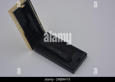 Cosmétiques pour femmes, choses, vieilles ombres à paupières noires et grises avec des pinceaux noirs emballés dans un emballage en plastique noir et or disposé sur fond blanc. Banque D'Images