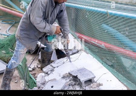 Ouvrier brisant le béton à l'aide d'un marteau-piqueur sur le chantier de construction. Banque D'Images