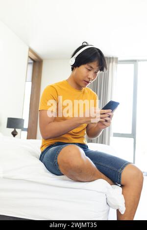 Adolescent asiatique aime la musique sur son téléphone à la maison, avec espace de copie Banque D'Images