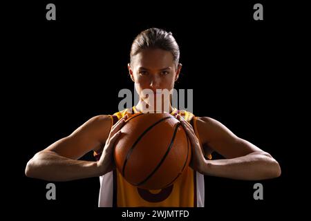 Joueuse de basket-ball féminine confiante prête pour le jeu, respire la force sur fond noir. Banque D'Images