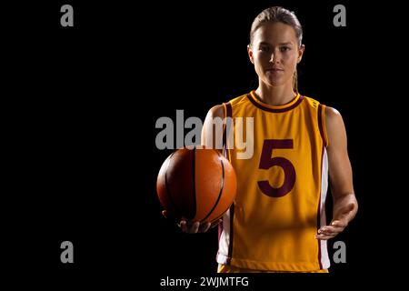 Femme athlétique en équipement de basket-ball pose avec concentration, mettant en valeur le dévouement. Banque D'Images