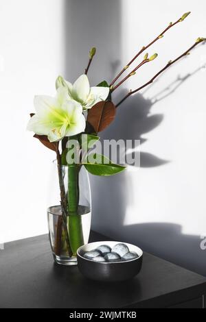 Bouquet printanier avec des branches et des feuilles de magnolia et d'amaryllis dans un vase en verre et des œufs gris de Pâques dans un bol sur la table. Joyeuses Pâques concept. Banque D'Images