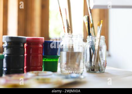 Une variété de pinceaux reposent dans un bocal sur la table d'un artiste Banque D'Images