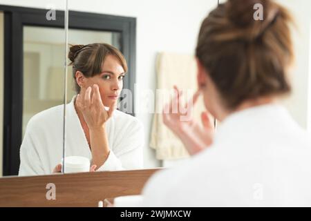 Femme caucasienne applique de la crème sur son visage à la maison Banque D'Images