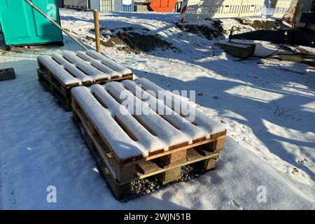 Des palettes en bois recouvertes de neige reposent sur un chantier de construction. Banque D'Images