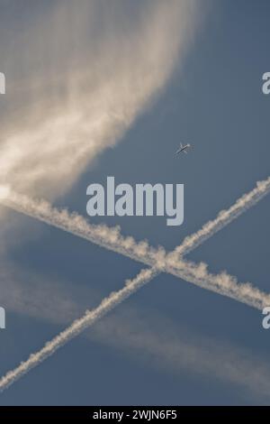 Avion/avion lointain dans le ciel bleu, avec nuage de whisky et traînées croisées. Banque D'Images