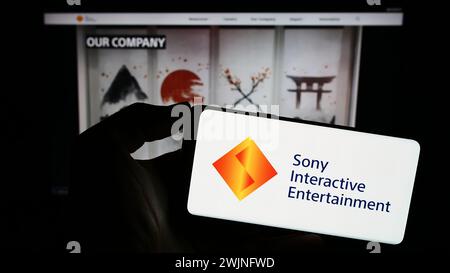 Personne tenant le téléphone portable avec le logo de la société américaine de jeux vidéo Sony Interactive Entertainment LLC en face de la page Web. Concentrez-vous sur l'affichage du téléphone. Banque D'Images