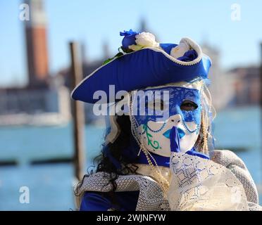 Venise, VE, Italie - 13 février 2024 : femme en masque et chapeau bleu avec le doigt sur les lèvres demandant le silence au bord de la mer Banque D'Images