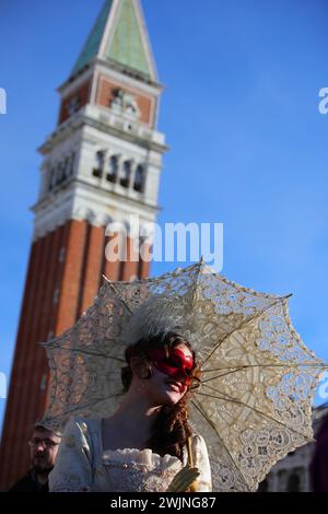 Venise, VE, Italie - 13 février 2024 : fille avec masque et rouge à lèvres rouge et parapluie et clocher pendant le Carnaval vénitien Banque D'Images