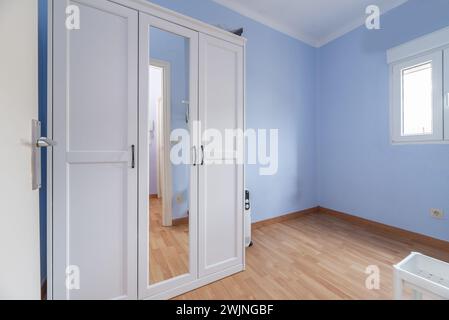 Chambre à moitié vide avec une armoire en bois blanc et une porte d'entrée avec un miroir Banque D'Images