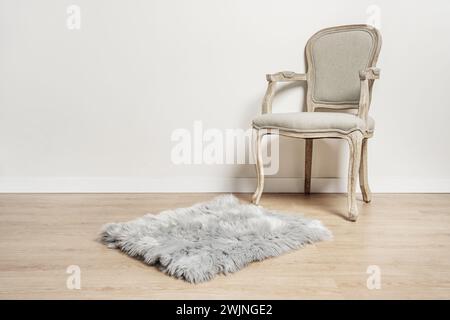 un fauteuil en bois clair non verni avec un siège rembourré gris, un tapis shag gris dans une pièce aux murs blancs et au parquet clair Banque D'Images