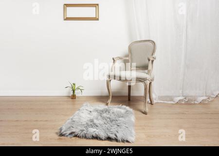 un fauteuil en bois clair non verni avec un siège rembourré gris, un tapis gris dans une pièce aux murs blancs et au parquet clair, une petite plante sur le sol Banque D'Images