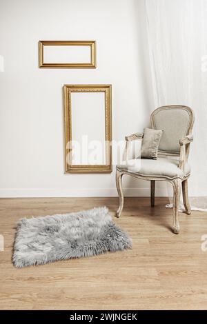 un fauteuil en bois clair non verni avec un siège rembourré gris, un tapis gris avec des rideaux blancs, des planchers en bois clair et une paire de fra en bois doré Banque D'Images