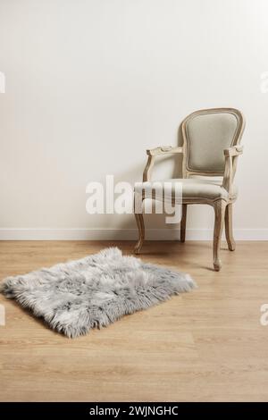 un fauteuil en bois clair non verni avec un siège rembourré gris, un tapis shag gris sur le plancher en bois clair et un mur blanc cassé uni Banque D'Images