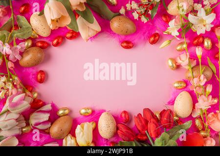 Cadre d'oeufs et de fleurs de printemps sur plumes roses avec des oeufs en chocolat rouge et or sur un fond rose Banque D'Images