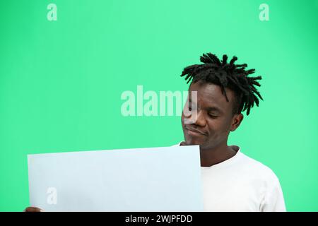 Un homme, en gros plan, sur fond vert, montre une feuille blanche. Banque D'Images