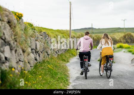 Deux touristes à vélo électrique sur Inishmore, la plus grande des îles d'Aran dans la baie de Galway, en Irlande. Louer un vélo est l'un des plus populaires Banque D'Images