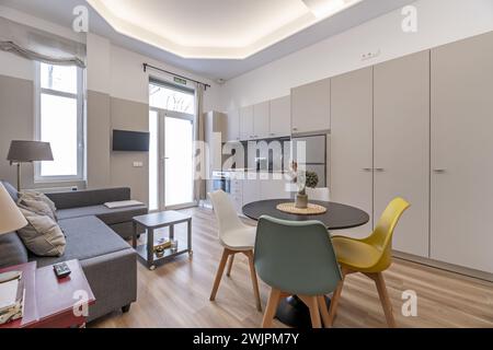 Petite maison de style loft avec canapé avec chaise longue tapissée de tissu gris foncé, porte d'accès avec verre translucide, salle à manger circulaire, cuisine Banque D'Images