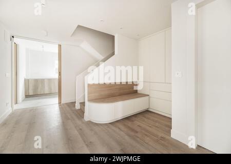 Hall d'entrée d'une maison unifamiliale avec un siège en bois avec de grands tiroirs en dessous à côté d'escaliers en briques peintes en blanc et beaucoup de lumière venant th Banque D'Images