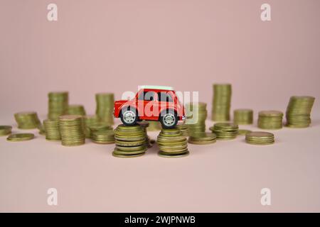 Jouet de voiture rouge sur des piles de pièces de monnaie. Fond rose. Banque D'Images