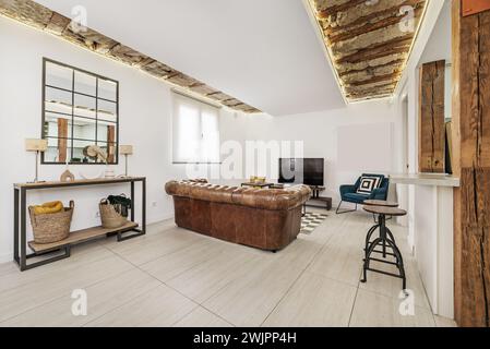 Un bel appartement loft avec un mobilier design contemporain, un buffet de style industriel avec un miroir et un canapé chesterfield regardant la télévision Banque D'Images