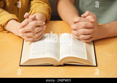 Couple de famille priant sur la Bible ensemble à table à l'intérieur, gros plan Banque D'Images