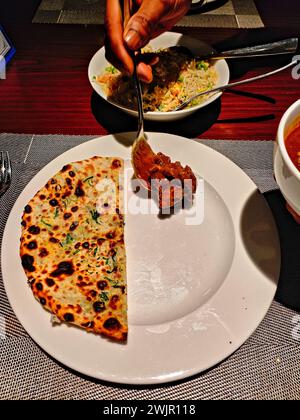 photo d'un naan au fromage à moitié tranché servi dans un plat blanc accompagné d'un curry de mouton Banque D'Images