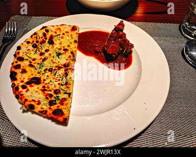 photo d'un naan au fromage à moitié tranché servi dans un plat blanc accompagné d'un curry de mouton Banque D'Images