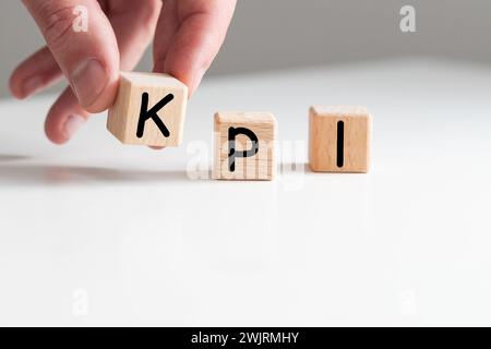 Gros plan sur la main du jeune homme dans le cube de bloc en bois de chemise blanche pour le libellé KPI sur le sol de la table en marbre blanc Banque D'Images