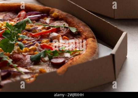 Grande Pizza avec saucisses poivrons et maïs doux dans une boîte de carton ouverte sur la table de cuisine vue rapprochée extrême Banque D'Images