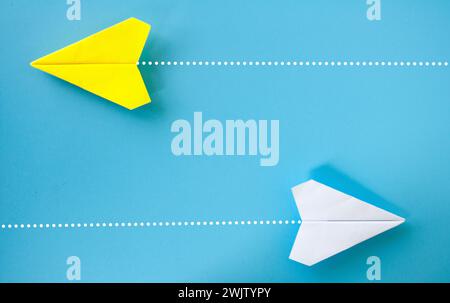 Vue de dessus d'origami d'avion de papier jaune et blanc volant dans une direction différente sur fond bleu. Banque D'Images