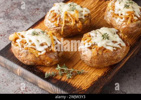 Pommes de terre en jaquette cuites au four farcies aux oignons caramélisés et au fromage gruyère gros plan dans un bol sur la table. Horizontal Banque D'Images