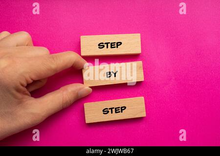 Étape par étape mots écrits sur des blocs de bois avec fond rose. Symbole conceptuel. Copier l'espace. Banque D'Images