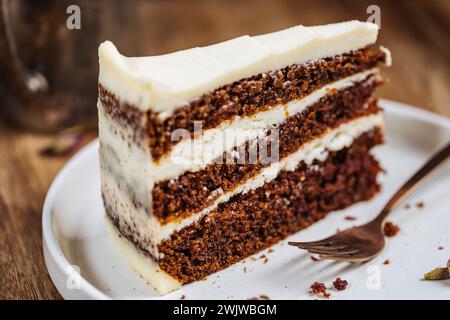 Un morceau de gâteau aux carottes servi sur un plateau en bois rustique. Scène ensoleillée lumineuse. Gâteau en couches avec glaçage au fromage à la crème et biscuit moelleux. Banque D'Images