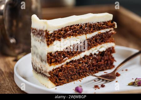 Un morceau de gâteau aux carottes servi sur un plateau en bois rustique. Scène ensoleillée lumineuse. Gâteau en couches avec glaçage au fromage à la crème et biscuit moelleux. Banque D'Images