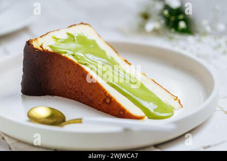 Dessert espagnol populaire appelé Saint-Sébastien cheesecake. gâteau au fromage brûlé basque. Un morceau de gâteau sur fond blanc avec glaçage à la pistache dessus. Banque D'Images