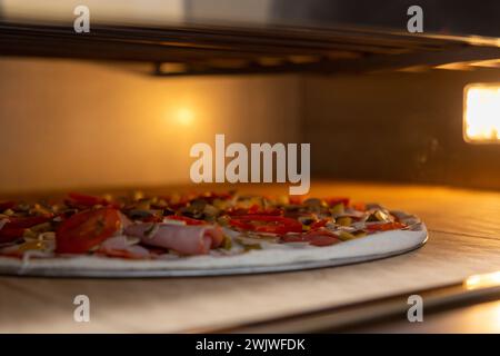 Pizza non cuite avec saucisse, jambon, champignon, poivre, tomates mozzarella au four électrique dans la pizzeria ou à la maison. Cuisine italienne, boulangerie maison, rapide f Banque D'Images
