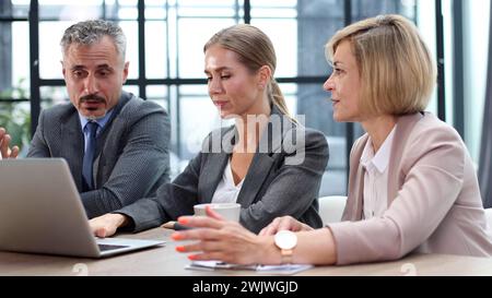 Assis près de la table avec des ordinateurs portables. Jeunes gens d'affaires travaillant au bureau Banque D'Images