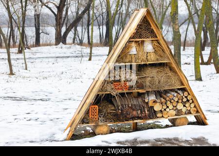 Hôtel d'insectes en paille, bâtons de bambou, briques, tuiles, galets de rivière, écorce d'arbre et tiges tubulaires dans un parc d'hiver sur la rive de la rivière. Banque D'Images