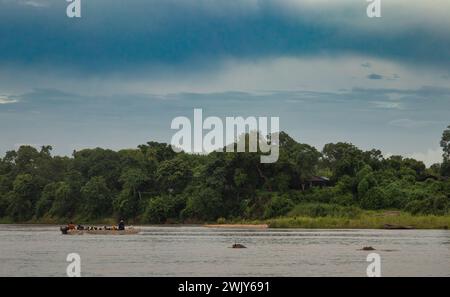 Les villageois passent devant deux hippopotames alors qu'ils utilisent un petit ferry pour traverser la rivière Rufiji à Mwaseni à l'intérieur du parc national Nyerere (réserve de gibier de Selous) à T. Banque D'Images